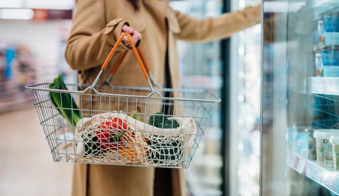 Cropped photo of a woman carrying a shopping basket and reaching into a refrigerated case in a supermarket